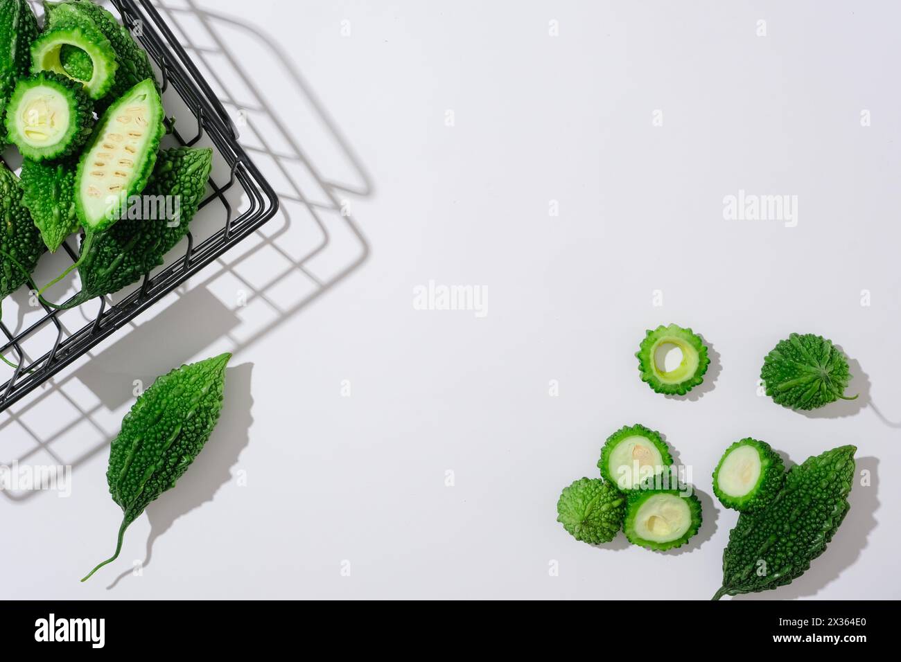 Fette fresche di melone amaro decorate su sfondo bianco e cesto nero. Scena minima di ingredienti naturali per cosmetici. Spazio vuoto per pro Foto Stock