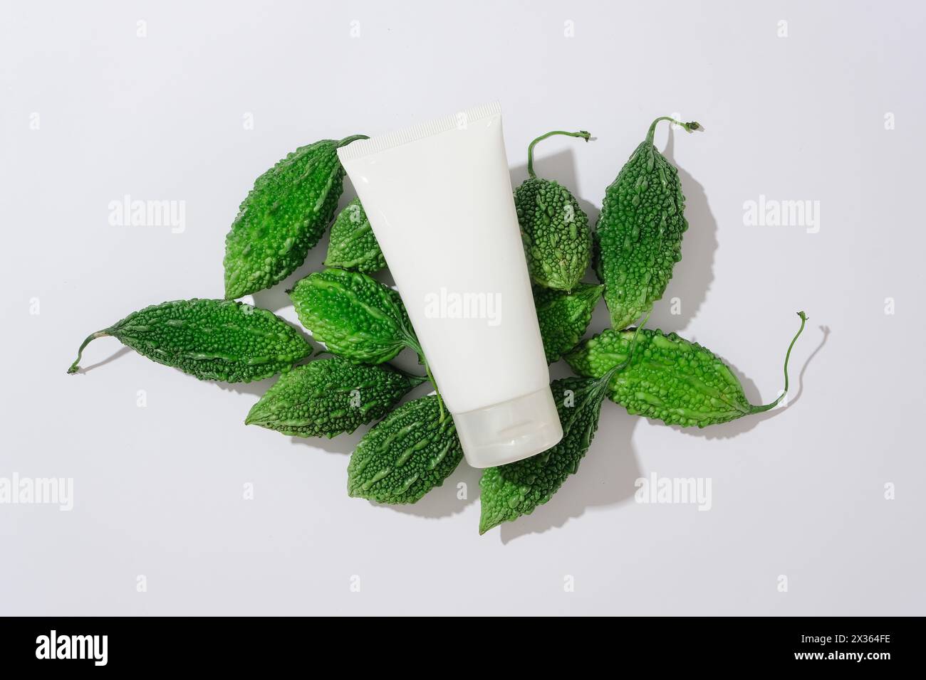 Vista dall'alto di un contenitore in plastica bianco con crema di detergente posizionato su melone amaro fresco su sfondo bianco. Scena minima per pubblicità, mockup Foto Stock