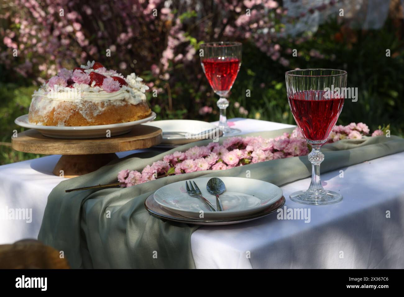 Splendidi fiori primaverili, deliziosa torta e bicchieri da vino sul tavolo in giardino Foto Stock