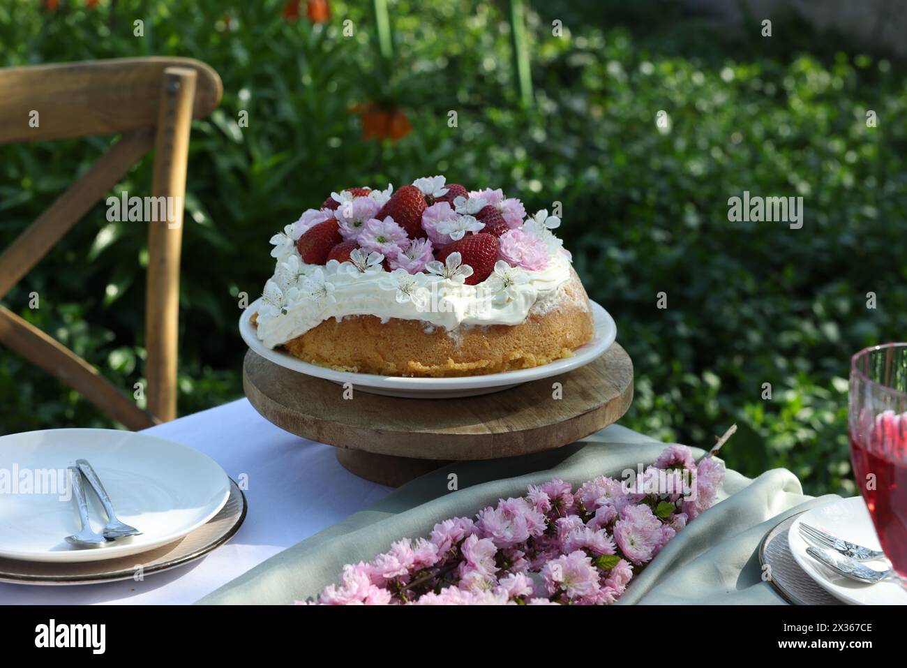 Bellissimi fiori primaverili e deliziosa torta sul tavolo in giardino Foto Stock
