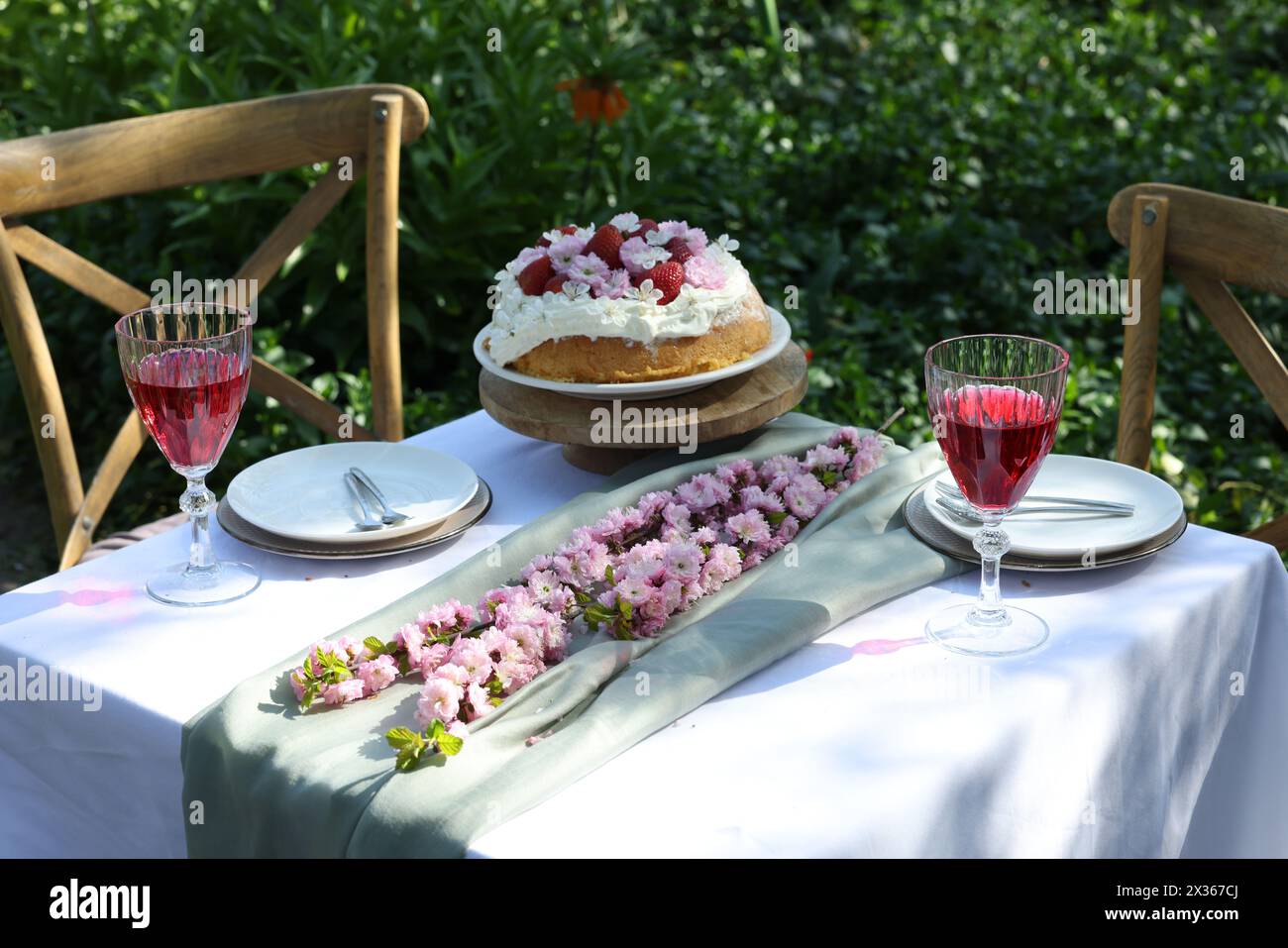 Splendidi fiori primaverili, deliziosa torta e bicchieri da vino sul tavolo in giardino Foto Stock