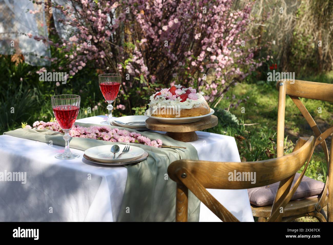 Splendidi fiori primaverili, deliziosa torta e bicchieri da vino sul tavolo in giardino Foto Stock