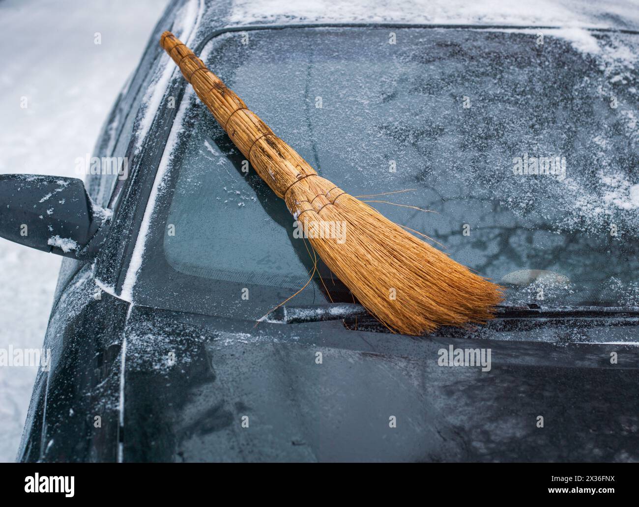 spazza via la neve con la scopa dal parabrezza di un'auto e il paesaggio invernale all'aperto Foto Stock