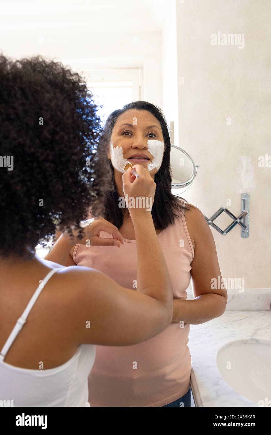 Maturo madre e figlia birazziale che applicano maschere facciali a casa in bagno Foto Stock