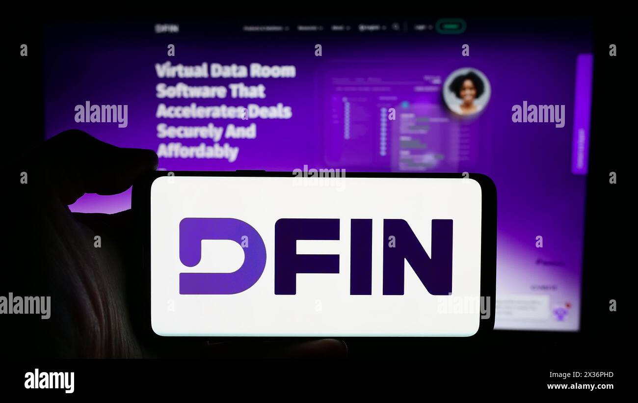 Persona che detiene un cellulare con il logo della società statunitense Donnelley Financial Solutions Inc. (DFIN) di fronte alla pagina Web aziendale. Mettere a fuoco il display del telefono. Foto Stock