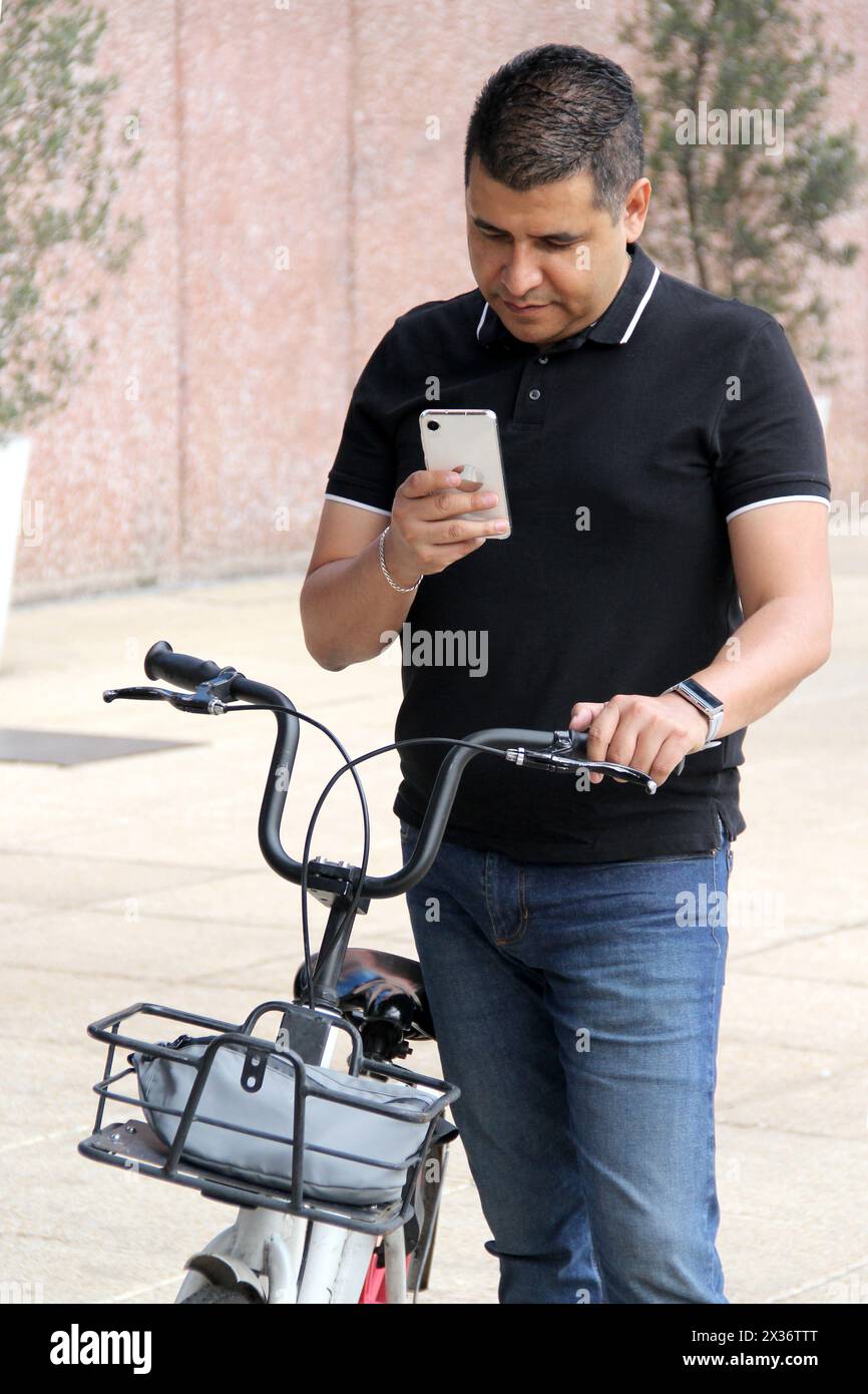 Un adulto latino dalla pelle scura usa l'app sul suo telefono per utilizzare le biciclette pubbliche della città come mezzo di trasporto sostenibile Foto Stock