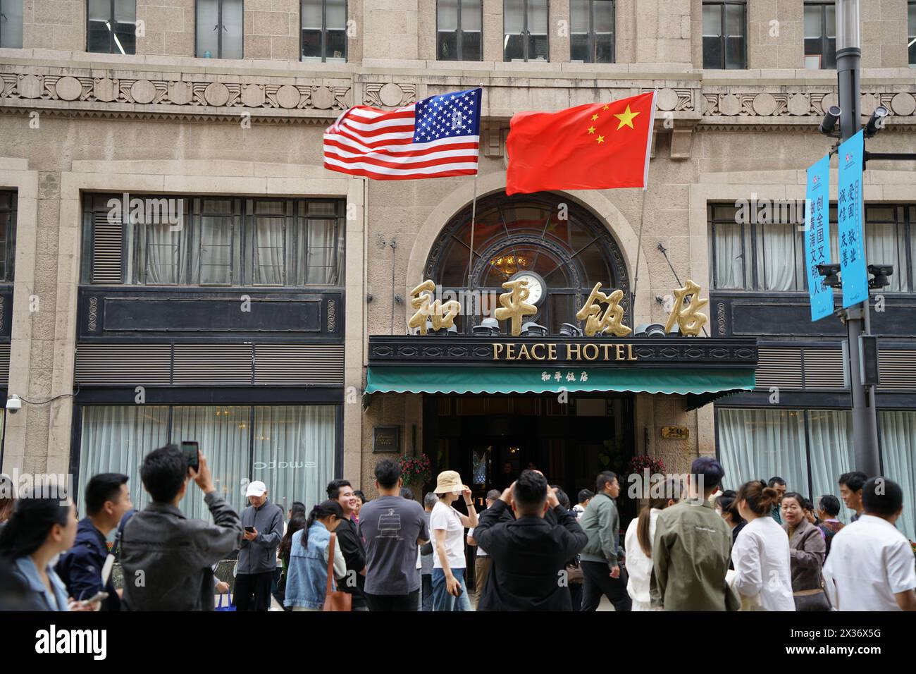 SHANGHAI, CINA - 25 APRILE 2024 - la bandiera rossa a cinque stelle della Cina e la bandiera degli Stati Uniti sono appese sopra l'ingresso del Peace Hotel lungo Nanjing Road Pede Foto Stock