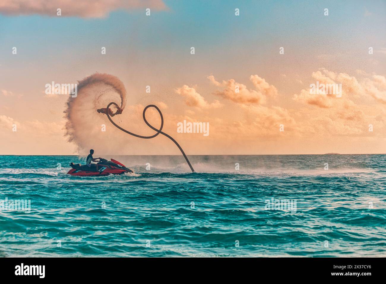 Silhouette di un pilota di fly board in mare. Il pilota professionista fa dei trucchi nella laguna blu. Attrezzature per sport acquatici tropicali. Vista mare al tramonto, estate all'aperto Foto Stock
