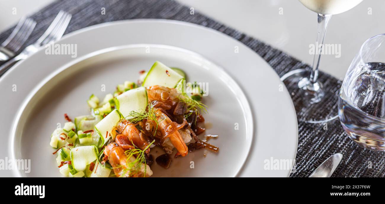Delizioso piatto di gamberi servito con verdure fresche su piatto bianco. Elegante antipasto di gamberi, arrotondati di cetrioli, guarniti con rametti di aneto freschi. Foto Stock