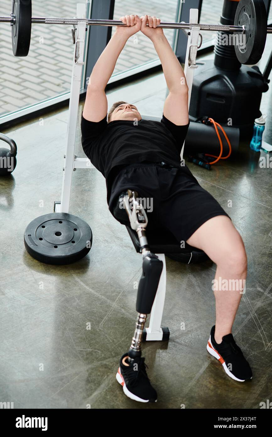Un uomo disabile con una gamba protesica che indossa una camicia nera esegue uno squat di barbell in una palestra. Foto Stock