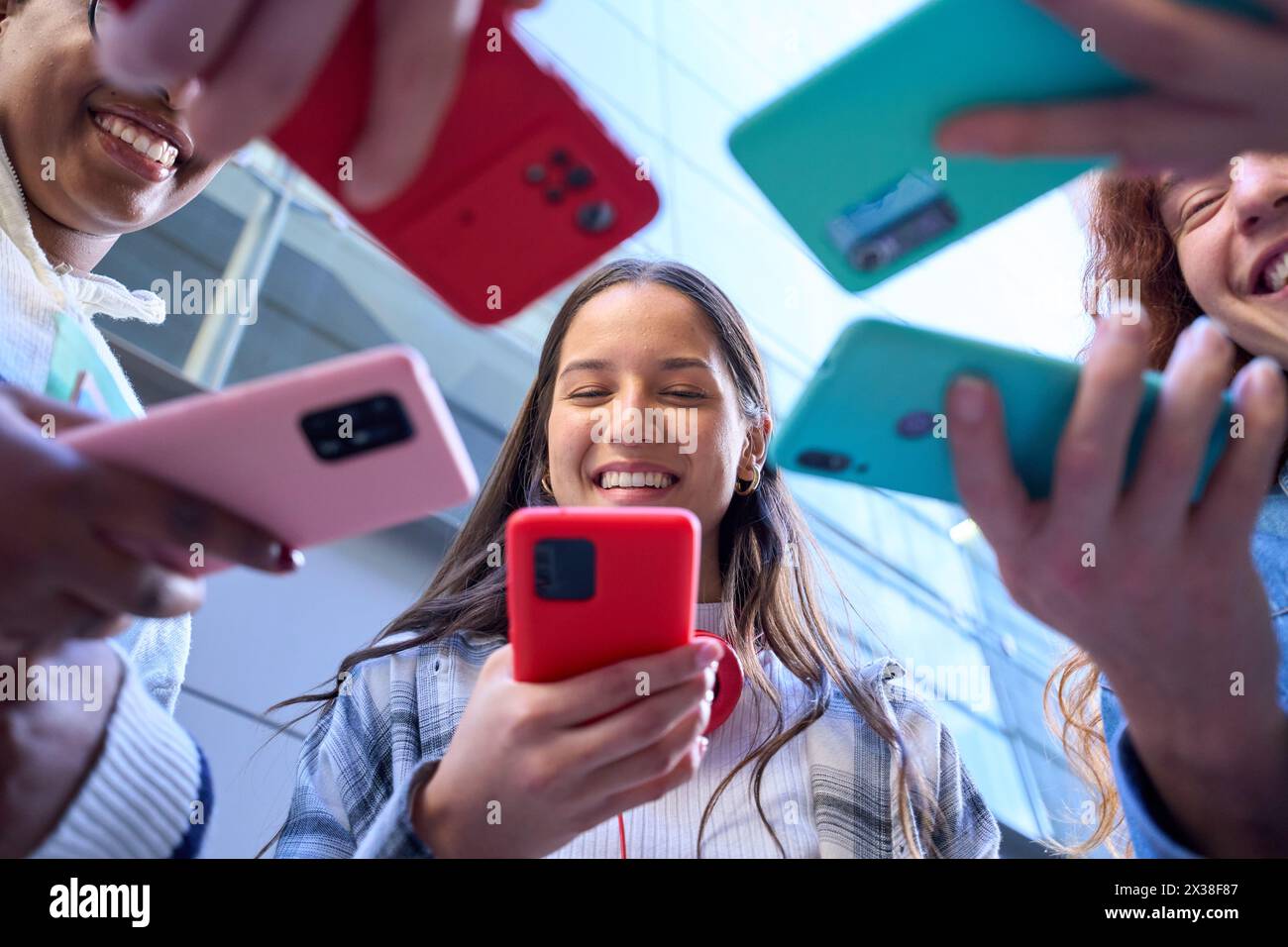 Angolo basso. Raggruppa giovani sorridenti in cerchio utilizzando cellulari colorati insieme all'esterno. Foto Stock