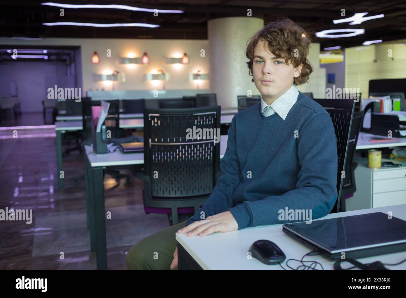 Un teenager seduto in un ufficio moderno con molti posti di lavoro Foto Stock