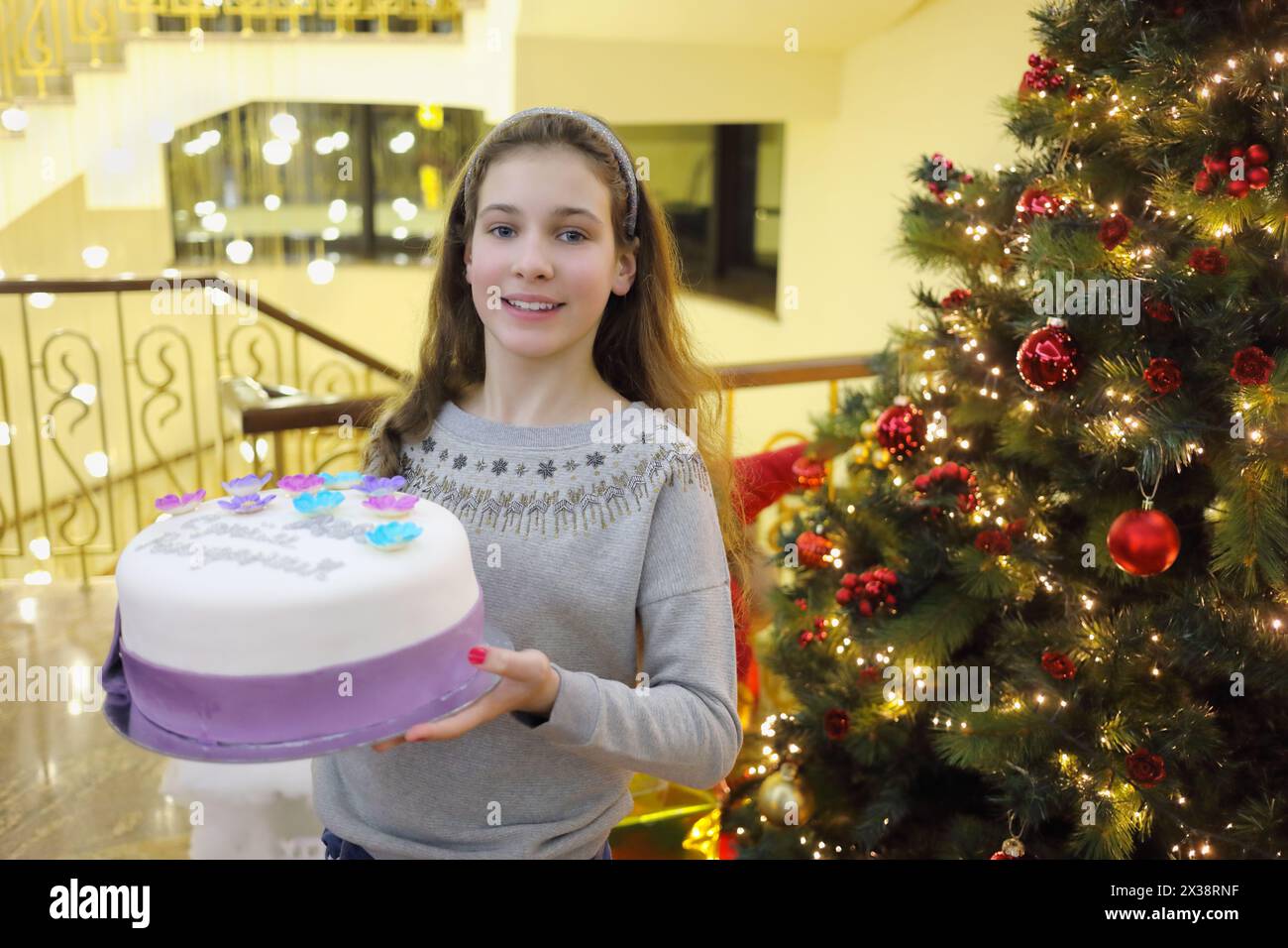 La bella ragazza tiene la torta dolce vicino all'albero della massa del battesimo, testo sulla torta - buon compleanno Anya Foto Stock