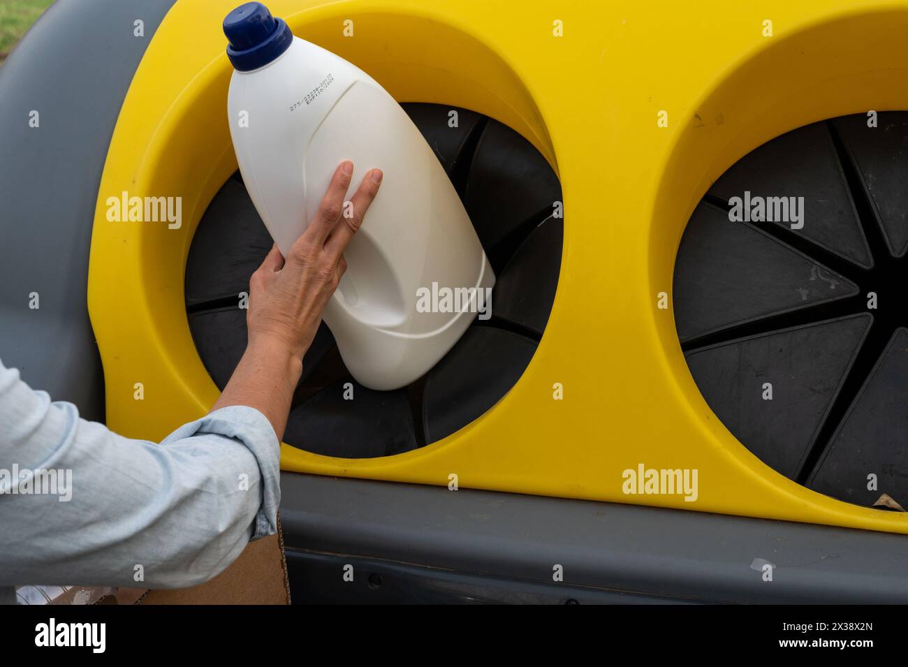 La mano di una donna che getta un contenitore in un bidone di rifiuti riciclabili. La tanica ha un coperchio giallo e un bordo nero Foto Stock