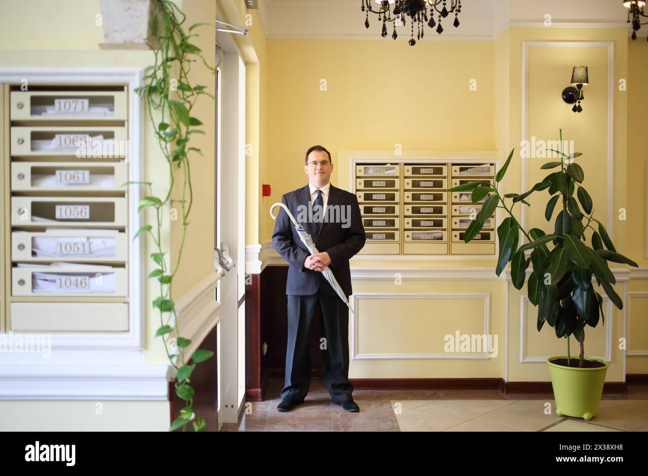 Bell'uomo con un costume da lavoro e cravatta in piedi con un ombrello argentato nel corridoio vicino all'ingresso Foto Stock