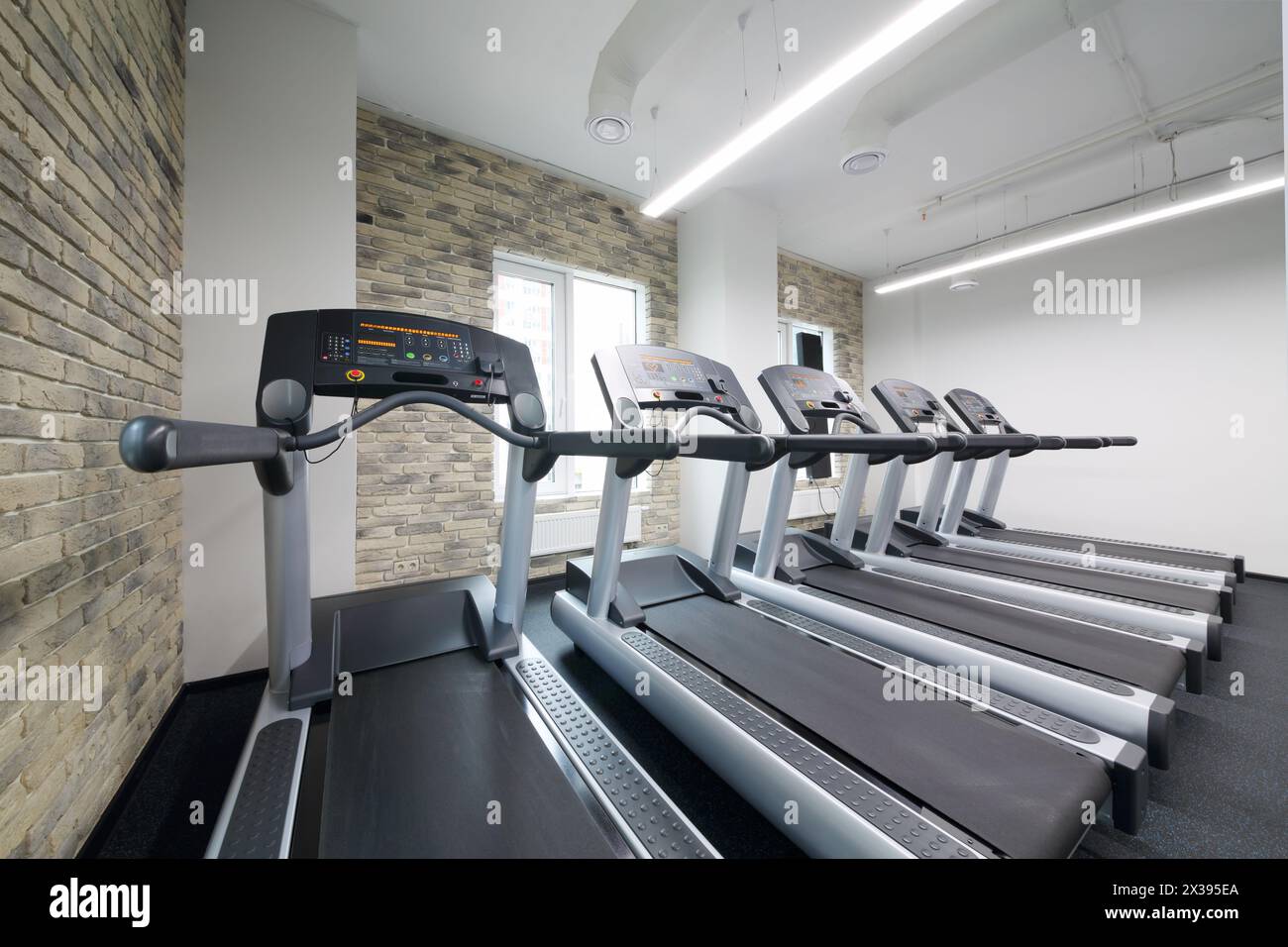 Cinque nuovi tapis roulant in una moderna sala vuota per il fitness con pareti in mattoni Foto Stock