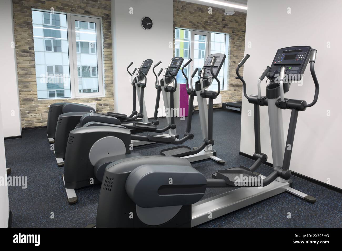 Quattro nuove macchine ellittiche in una moderna sala vuota per il fitness con pareti in mattoni Foto Stock