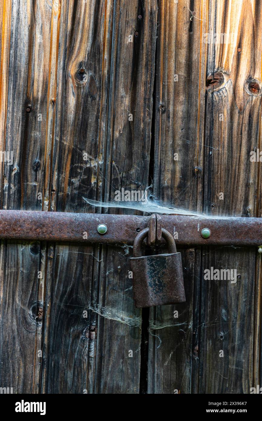 Vista ravvicinata del vecchio lucchetto arrugginito su una vecchia porta di legno grigio. Foto Stock
