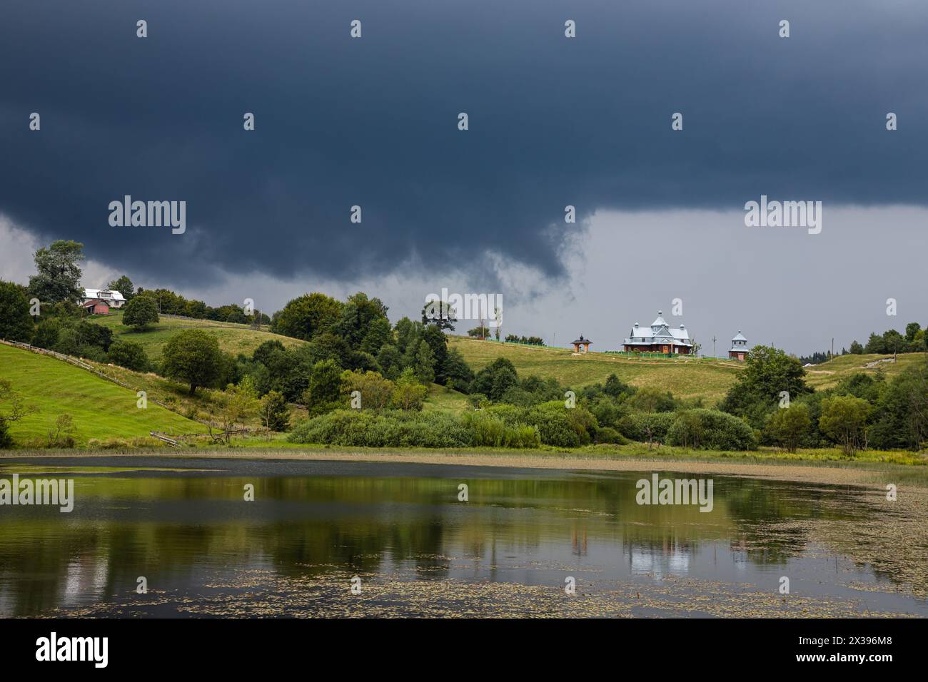 Nuvole tempesta, cielo minaccioso, collina e chiesa, alberi verdi prima della pioggia. Foto Stock
