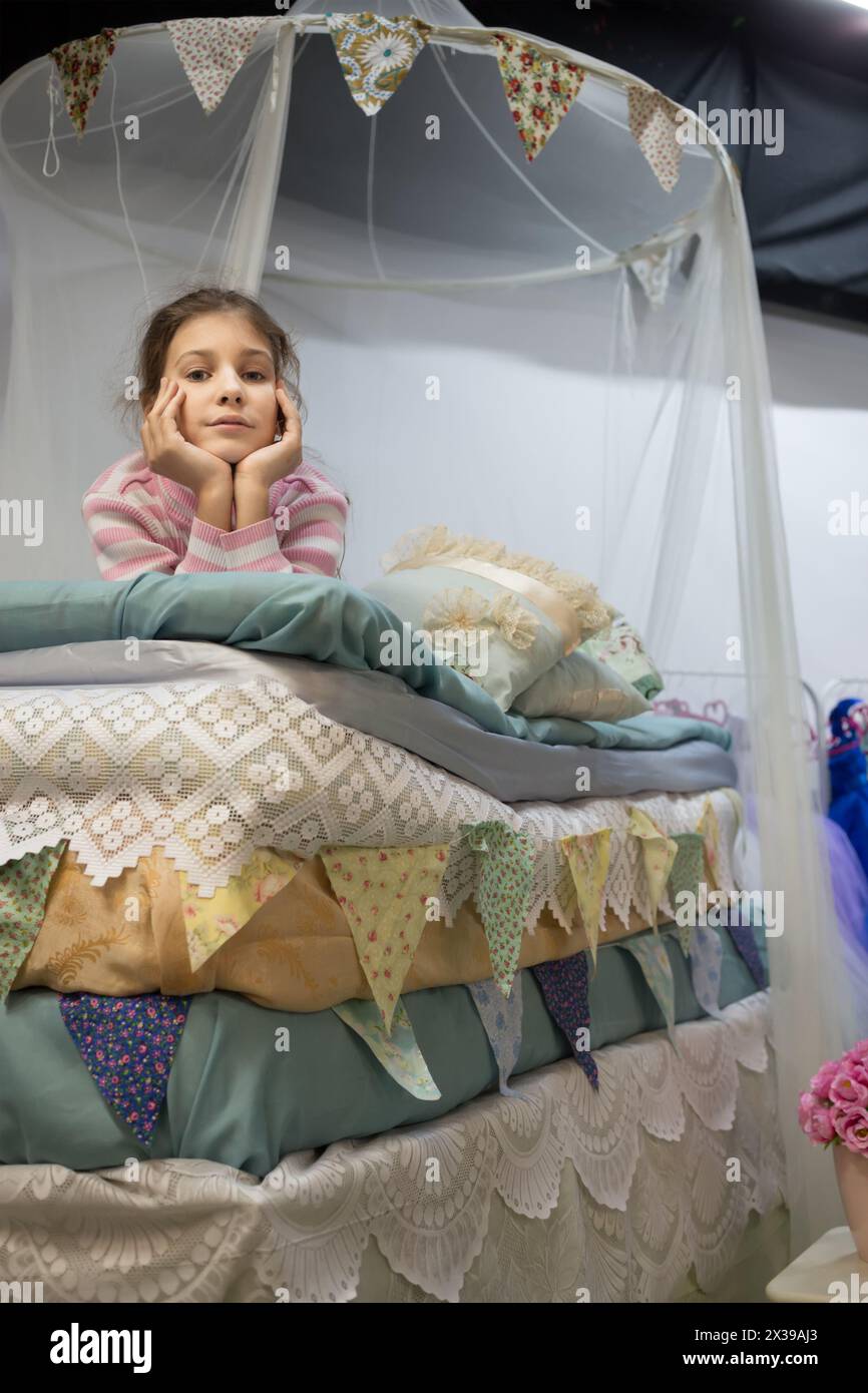 Una bambina sta sdraiata sui molti materassi sotto una tenda del letto. Foto Stock