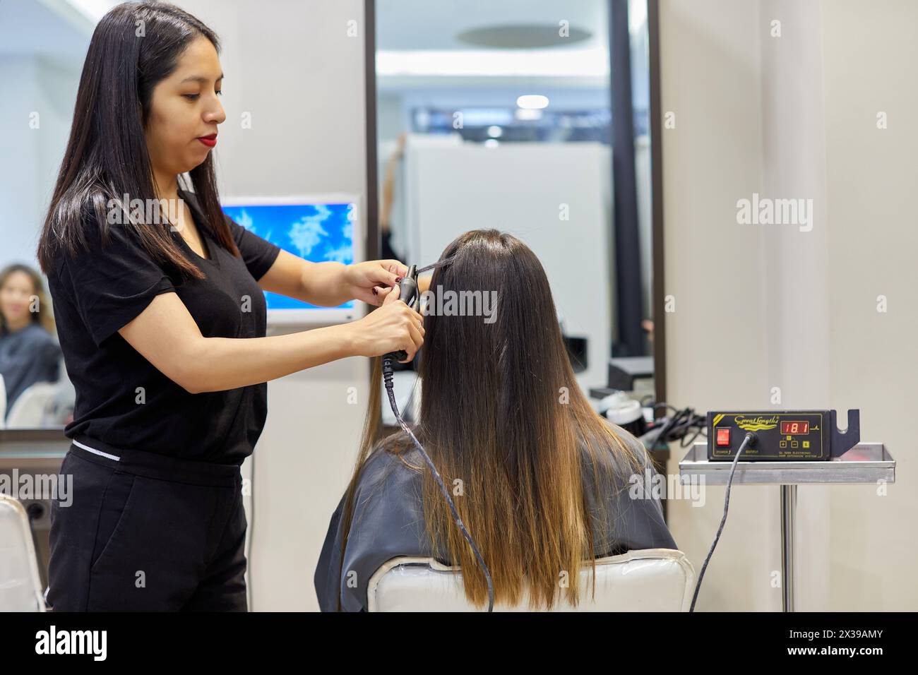 Parrucchiere che mette le estensioni dei capelli ad una donna, salone di parrucchiere e clinica di bellezza. Foto Stock