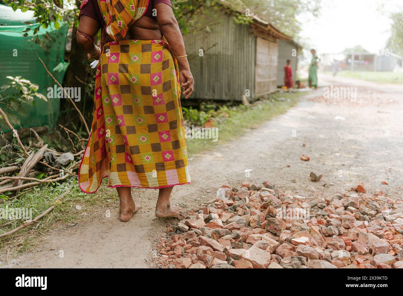 Vecchia donna indiana in sari tradizionali che cammina su una strada sterrata in un villaggio nell'India rurale. Concetto di povertà, infrastrutture e sviluppo dell'India Foto Stock