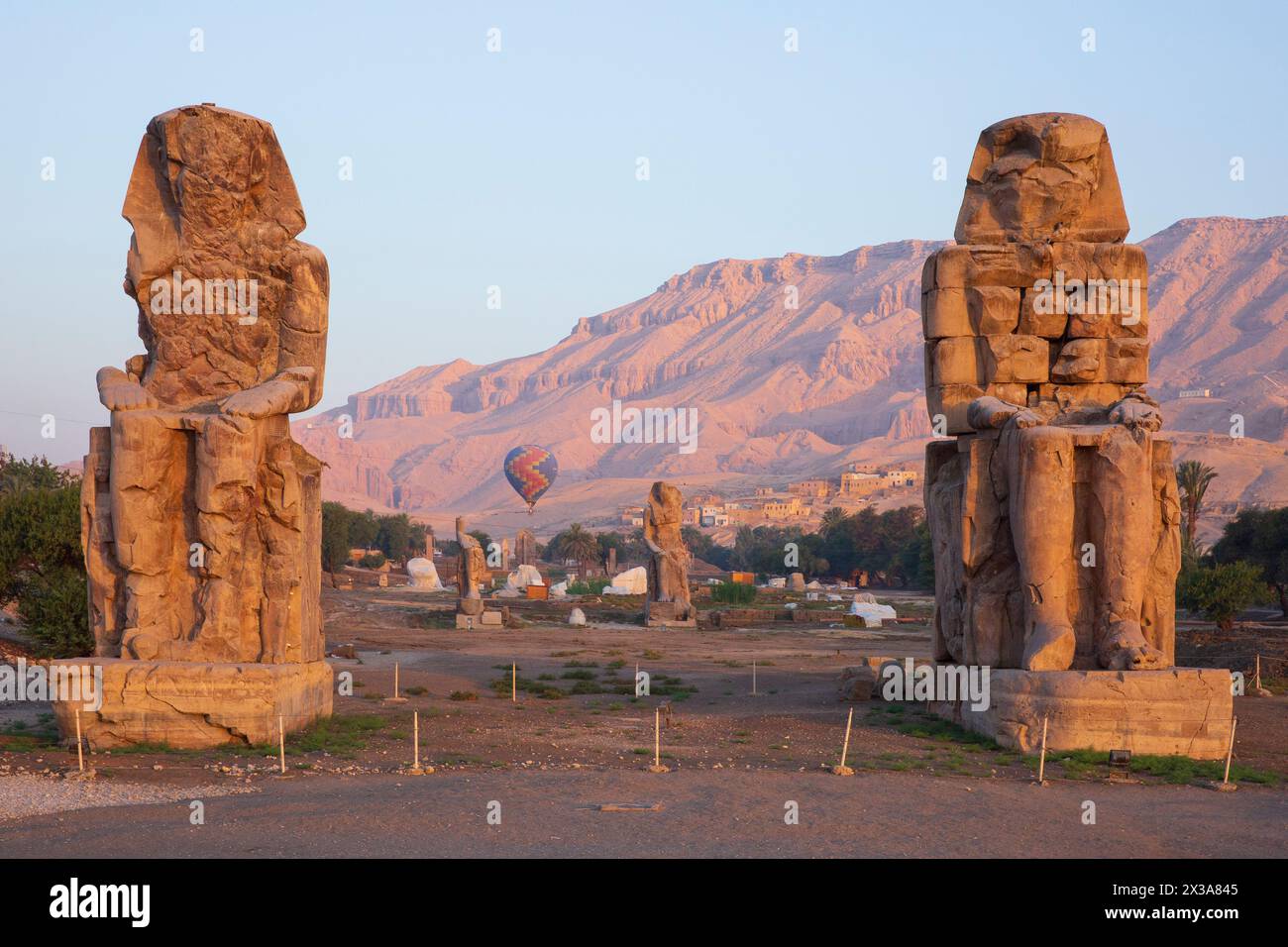 Una colorata mongolfiera sorvolando i Colossi di Memnone all'alba sulla sponda occidentale di Luxor, in Egitto Foto Stock