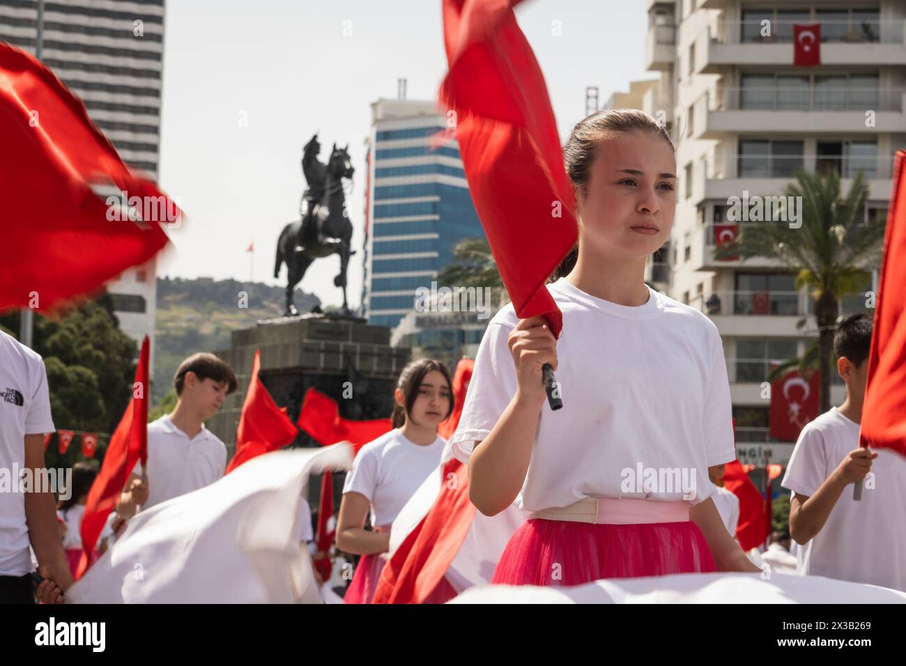 Izmir, Turchia - 23 aprile 2024: Una vista ravvicinata di un giovane studente che detiene una bandiera turca, con gli altri partecipanti che sventolano bandiere sullo sfondo, du Foto Stock