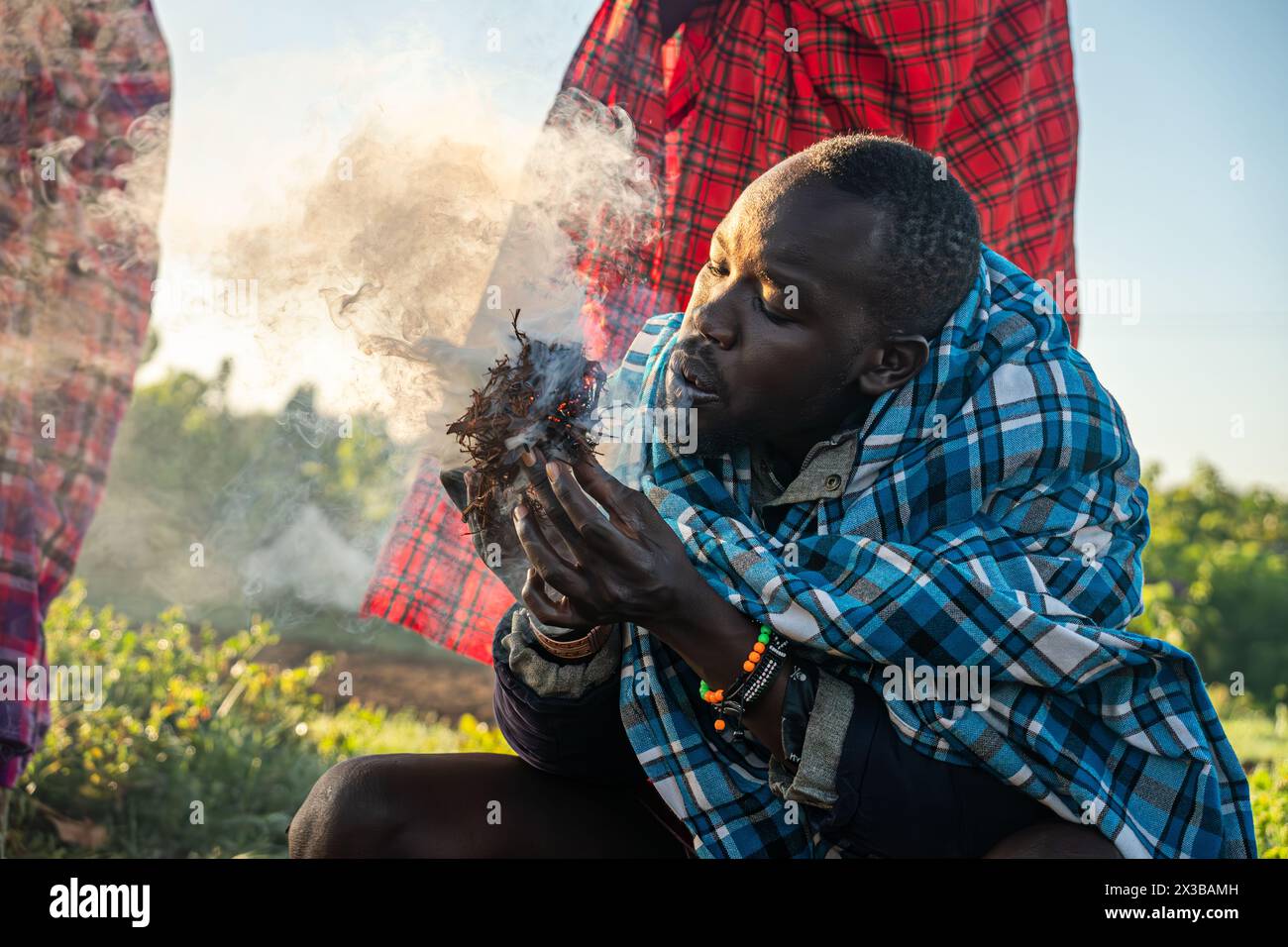 4 febbraio 2024. Villaggio di Masai in Kenya.: Un uomo masai che dimostra una tecnica tradizionale di illuminazione del fuoco, soffiando sull'erba secca dopo che ha preso fuoco. Foto Stock