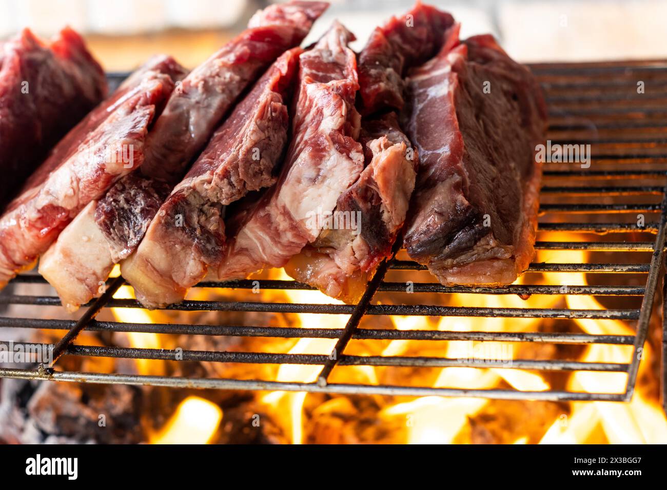 Vista ravvicinata di pezzi di carne cruda tagliati come bistecche su una griglia con il fuoco che brucia sotto Foto Stock