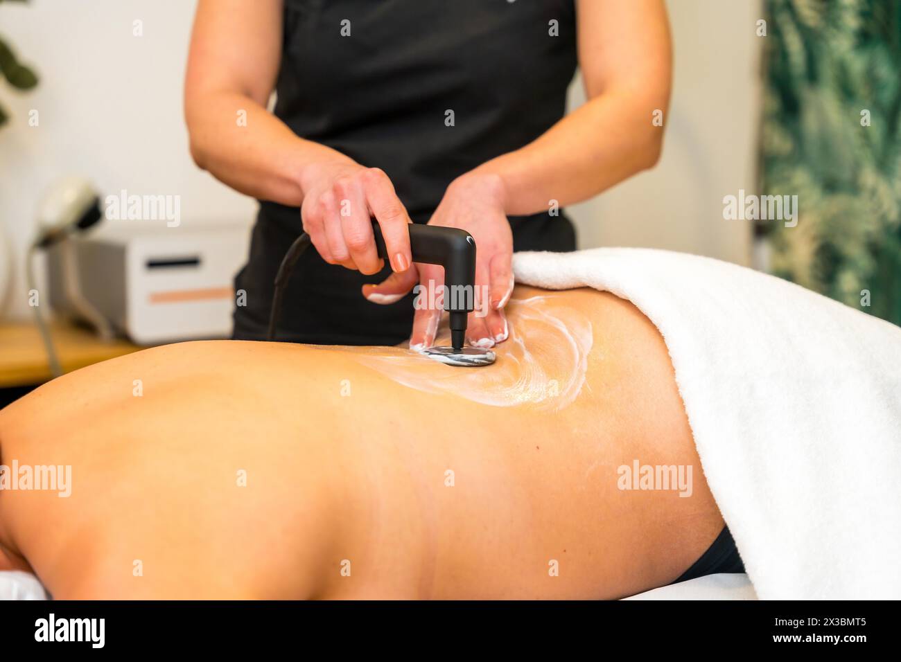 Primo piano di un fisioterapista non riconoscibile che utilizza lo strumento elettrico INDIBA per esercitare pressione sulla schiena di un paziente Foto Stock