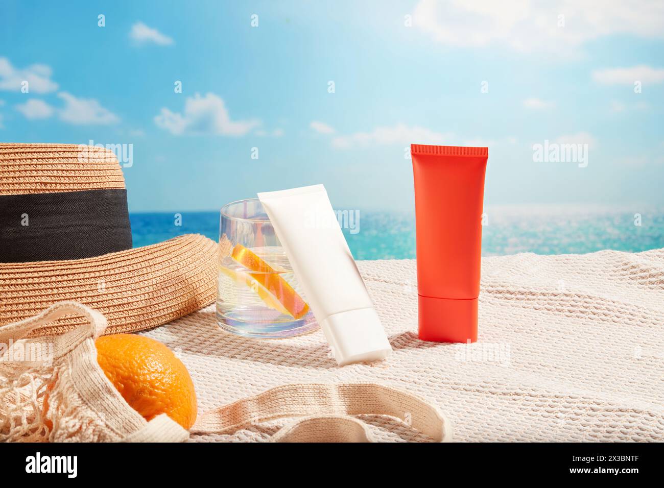 Tubi per crema solare in diversi colori esposti sulla sciarpa con una tazza d'acqua, un cappello da spiaggia e una borsa a rete di arance. Concetto cosmetico con protezione solare Foto Stock