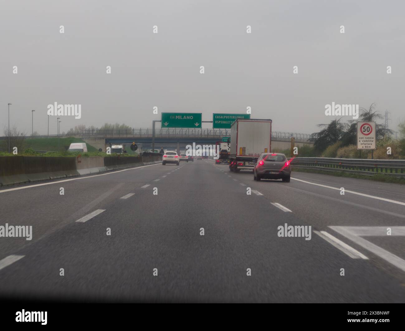Traffico su un'autostrada con una varietà di veicoli e cartelli stradali sotto un cielo grigio, autostrada A1 A8 vicino a Milano, Italia, Europa Foto Stock