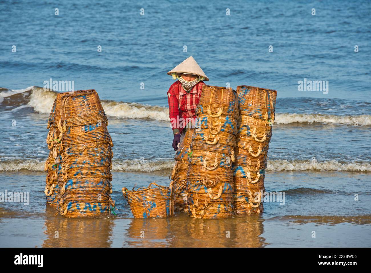 Donne con cappelli di paglia sulla spiaggia che puliscono i cesti per i pesci appena pescati e i frutti di mare, vicino al mare vicino a Mui ne, Phan Thiet, Vietnam Foto Stock