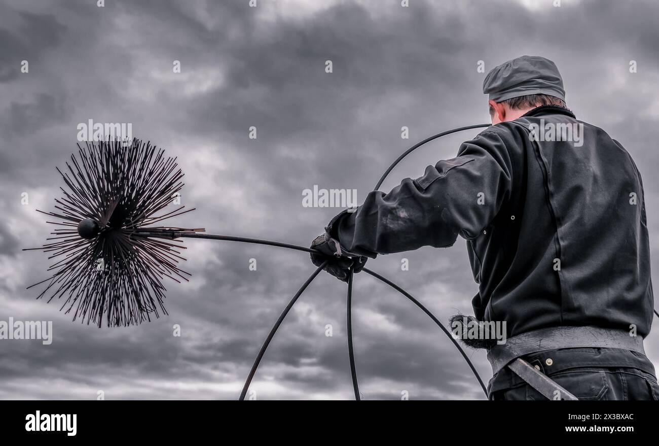 Un spazzacamino su un tetto, che pulisce il camino con una spazzola tradizionale montata su un'asta flessibile. Foto Stock