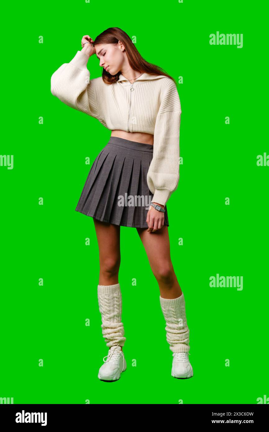 Giovane donna con maglione bianco e gonna grigia in piedi su sfondo verde Foto Stock