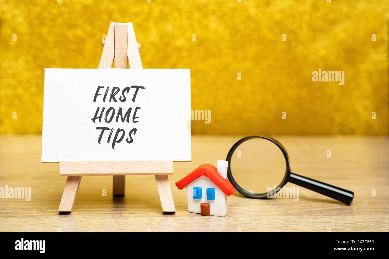 Concetto di First Home Tips. Consigli e orientamenti rivolti a persone che acquistano la loro prima casa. Casa in miniatura e lente d'ingrandimento Foto Stock