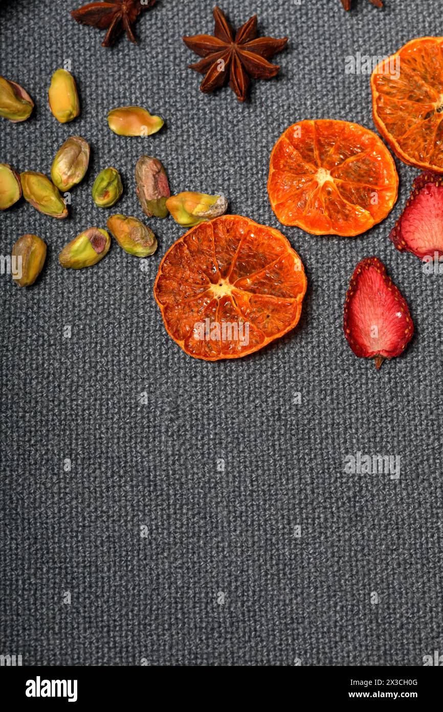 Mandarini e fragole essiccati, tagliati a pezzi per decorare il dessert. Nelle vicinanze ci sono pistacchi e anice. Su sfondo grigio. Foto Stock