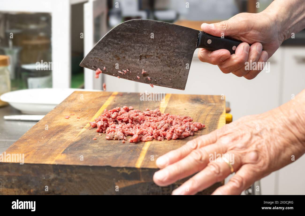 Cuocere il manzo crudo tagliato con un rasoio da cucina rustico su un blocco di legno per preparare tartare, carne macinata o macinata, copiare spazio e selezionare la messa a fuoco Foto Stock