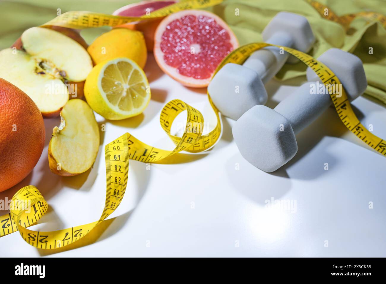 Agrumi freschi, mele, metro e manubri, concetto per uno stile di vita sano con fitness, sport e cibi ricchi di vitamine, bac grigio chiaro Foto Stock