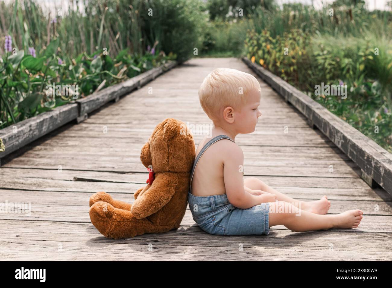 Bambino e orsacchiotto condividono un momento su una passerella di legno Foto Stock