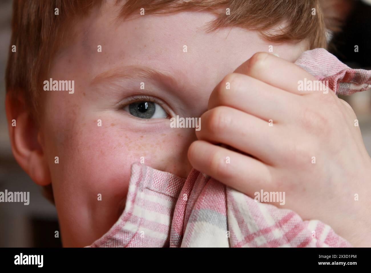 Bambino dai capelli rossi che si nasconde giocosamente dietro un tovagliolo a righe Foto Stock