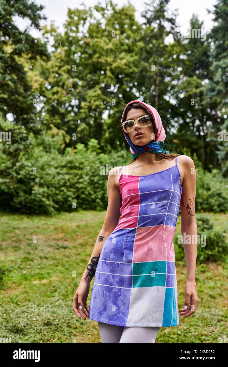 Una bella giovane donna con un abito vivace e occhiali da sole, che gode della brezza estiva in natura. Foto Stock