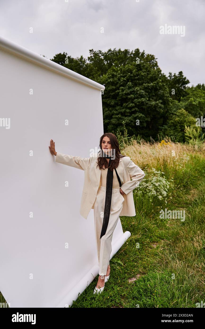 Una giovane donna in abito bianco si appoggia su un muro bianco, abbracciando la brezza estiva in un ambiente tranquillo. Foto Stock