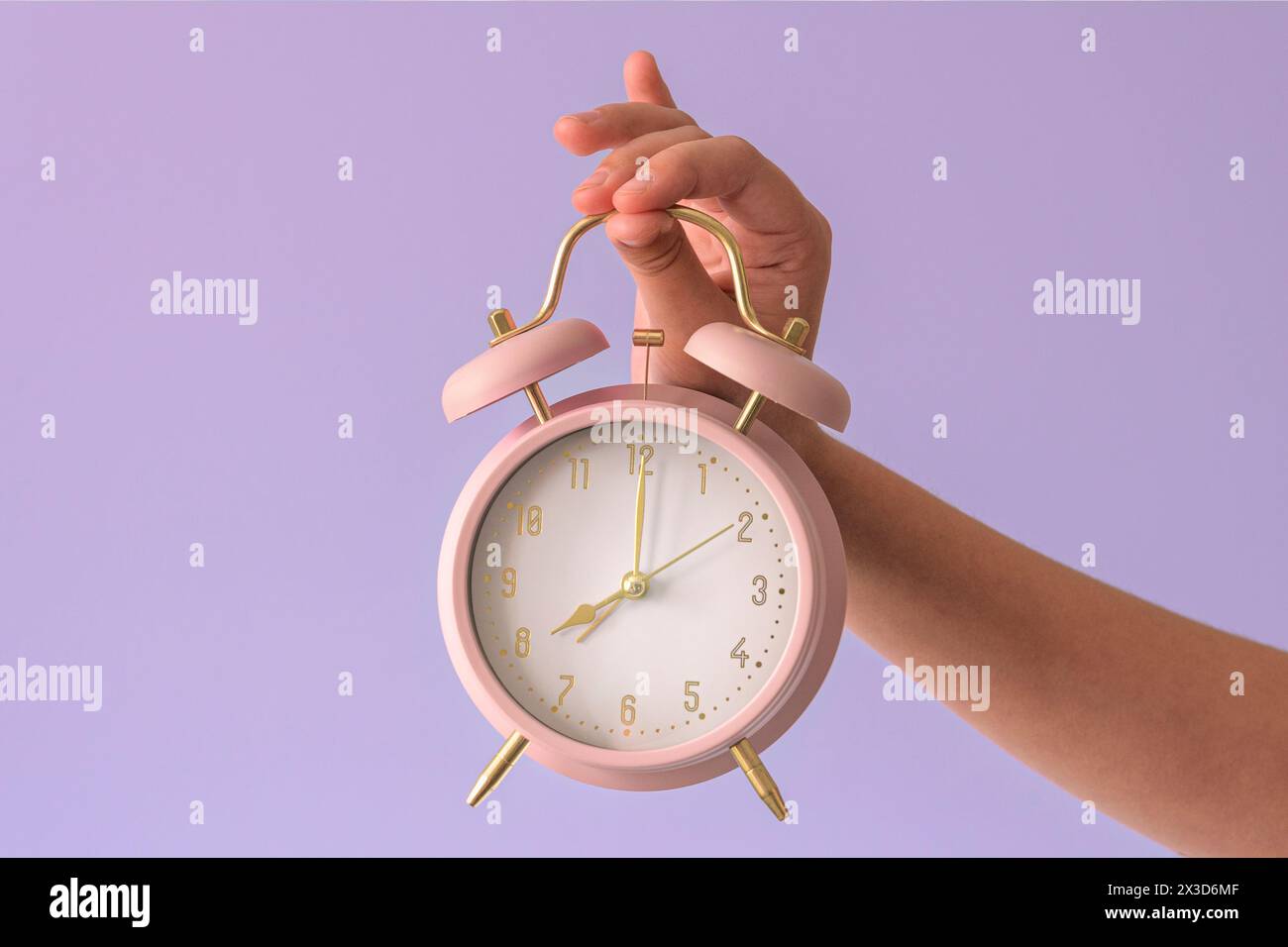 Sveglia in mano a un bambino. Otto ore, primo piano, sfondo rosa tenue Foto Stock