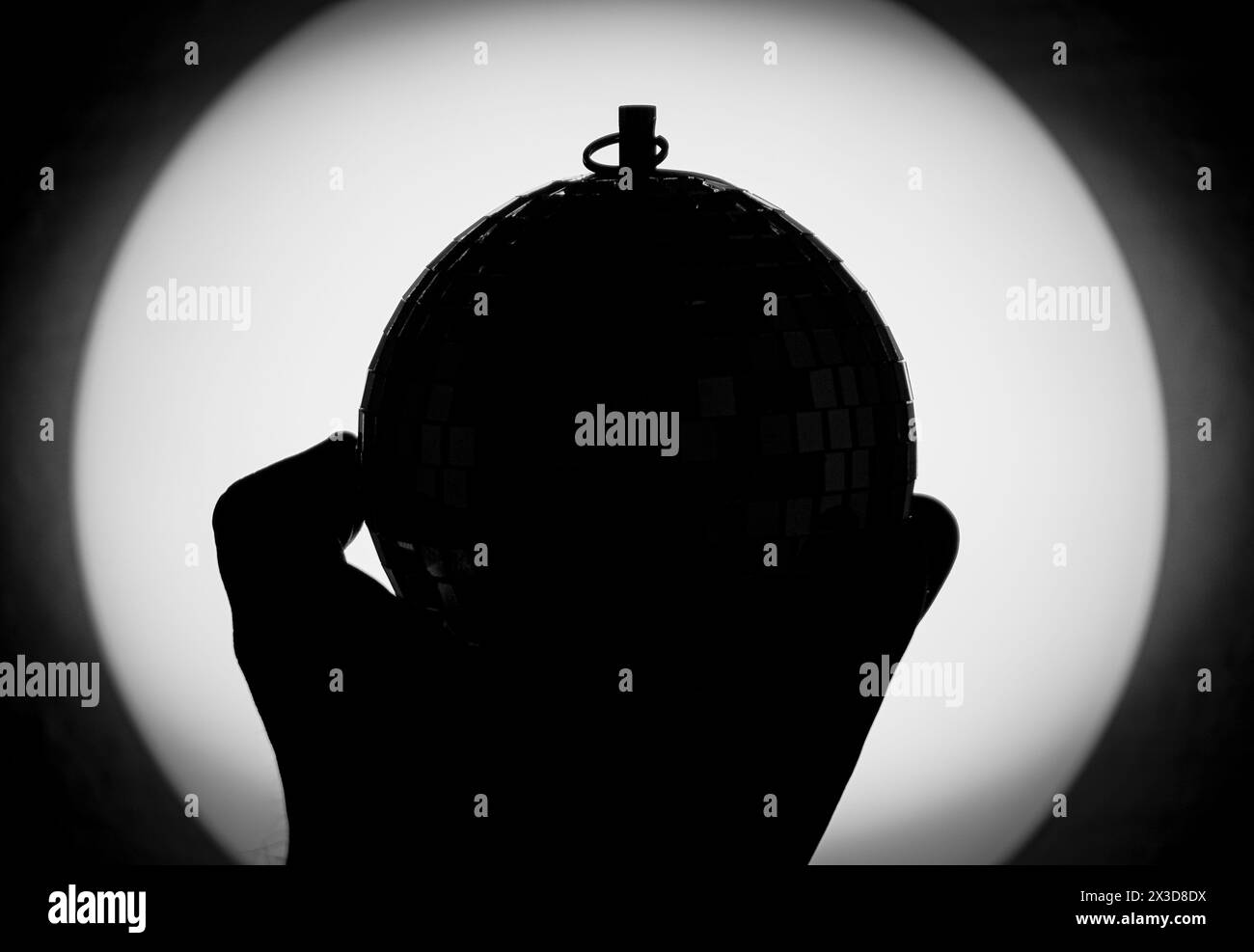 sagoma della mano che tiene la palla da discoteca contro la sorgente luminosa Foto Stock