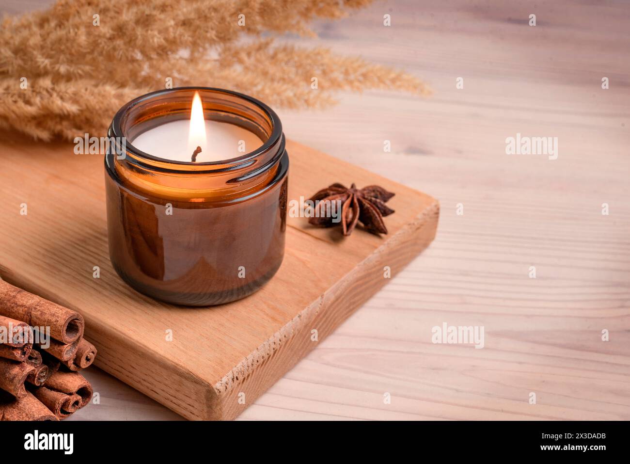 Massaggia candela bruciata profumata in vaso di vetro ambrato, arredi per interni in hygge invernale su vassoio di legno con bastoncini di cannella e anice, spazio per fotocopie. Cera di soia Foto Stock
