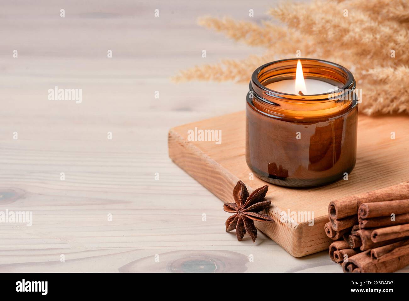 Massaggiate la candela bruciata profumata nel vaso di vetro ambrato, gli interni della casa in hygge invernale su un tavolo di legno con bastoncini di cannella e anice, spazio fotocopie. Soia wa Foto Stock