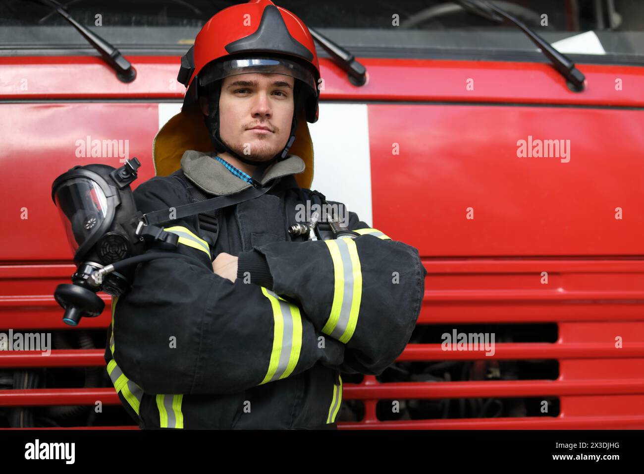 Ritratto di un pompiere che indossa i proiettili del fuoco e il casco rosso, piega le braccia Foto Stock