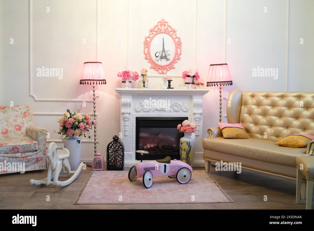L'interno del soggiorno è in stile romantico con caminetto, due lampade da terra rosa, un divano e un'auto retrò per bambini e cavallo in legno Foto Stock
